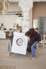 Vista lateral de descalzo contenido hombre y mujer llevando lavadora blanca mientras se muda a nueva casa - foto de stock