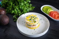 De arriba sabroso apetitoso Lima causa de atún decorado con tomates verdes y cocidos de aguacate en platos blancos sobre la mesa. - foto de stock