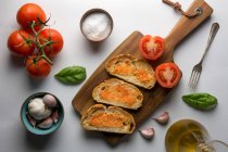Різні спеції і стиглі помідори поміщають на обробну дошку біля шматків хліба з соусом на білому тлі — стокове фото