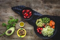 Zucchini raw vegan pasta with peas, cherry tomatoes, avocado, carrots,nuts and olive oil in bowl served on wooden background — Stock Photo
