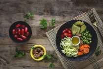Zucchini raw vegan pasta with peas, cherry tomatoes, avocado, carrots,nuts and olive oil in bowl served on wooden background — Stock Photo