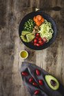 Pastas veganas crudas de calabacín con guisantes, tomates cherry, aguacate, zanahorias, nueces y aceite de oliva en un tazón servido sobre fondo de madera — Stock Photo