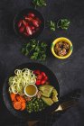 Zucchine crude vegane con piselli, pomodorini, avocado, carote, noci e olio d'oliva in ciotola servite su fondo scuro — Foto stock