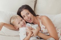 Удовлетворенная брюнетка обнимает счастливого малыша-сына на кровати — стоковое фото