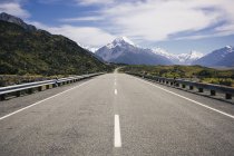 Асфальт дороги і тропічних зелених скель і блакитного озера з хмарним блакитним небом і гірським куком в Новій Зеландії. — стокове фото