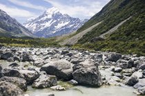 Rocky river among green cliffs with mountain Cook and sky at New Zealand — Stock Photo