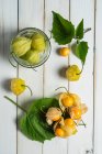 Сверху фрукты Физикалиса с листьями и стеклянной банкой на деревянных досках белого стола . — стоковое фото