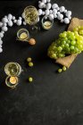 Silvesterfeier mit Weingläsern mit Champagner und rapsgrünen Trauben auf Tisch mit Teelichtern und weißem Kranz auf schwarzem Hintergrund — Stockfoto