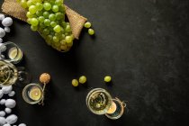 Celebração de Ano Novo com vinhedos com champanhe e uvas verdes de estupro na mesa decorada com velas de chá e guirlanda branca no fundo preto — Fotografia de Stock