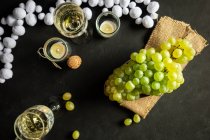 Celebración de Año Nuevo con copas de vino con champán y uvas verdes de colza en la mesa decoradas con velas de té y guirnalda blanca sobre fondo negro - foto de stock