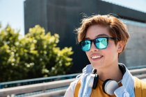 Яскрава тисячолітня жінка в стильних сонцезахисних окулярах насолоджується видом на міську вулицю — стокове фото