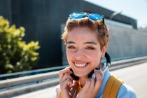Magnificent stylish millennial woman with headphones and sunglasses looking in camera against blurred road — Stock Photo