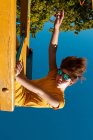 Знизу модний підліток в сонцезахисних окулярах грає на жовтій поперечині на прозорому блакитному небі — стокове фото
