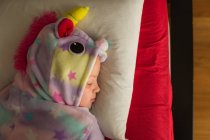 Chica en pijama unicornio durmiendo en la cama en casa - foto de stock