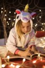 Mädchen liest Buch im Schlafzimmer mit Weihnachtsbeleuchtung dekoriert — Stockfoto