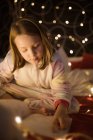 Girl reading book in bedroom decorated with Christmas lights — Stock Photo