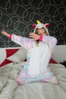 Веселая девушка в пижаме единорога веселится и прикрывает лицо на кровати — стоковое фото