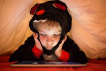 Маленький дошкольник использует планшет под одеялом в постели — стоковое фото
