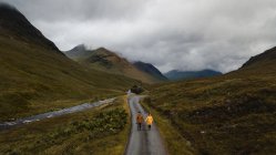 Вище подружжя насолоджується видом на порожню дорогу і тримається за руки біля гірської річки на зелених буйних луках Шотландії. — стокове фото