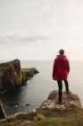 Turista solitario in piedi sulla costa rocciosa contro le acque tranquille del mare sotto il cielo grigio in Scozia — Foto stock