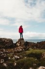 Turista solitario parado en la costa rocosa contra el agua de mar tranquila bajo el cielo gris en Escocia - foto de stock