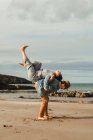 Side view of man holding on back laughing woman with raised legs on sandy beach with rocks on cloudy daytime in Scotland — Stock Photo