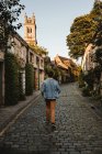 Visão traseira do viajante masculino andando na rua estreita com edifícios antigos e estrada de pedras de pavimentação na cidade escocesa — Fotografia de Stock