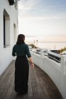 Vista posteriore della giovane donna che cammina sul balcone con pavimento in legno in città sul mare — Foto stock