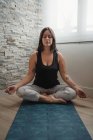 Молода жінка сидить у позі лотоса на килимок йоги і медитує під час занять ранковою йогою вдома — стокове фото