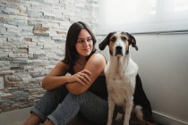 Young cheerful woman sitting with friendly mixed breed dog on floor at home — Stock Photo