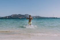 Человек в купальнике, бегущий в воде по берегу моря — стоковое фото