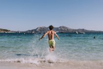 Hombre en traje de baño corriendo en el agua en la orilla del mar - foto de stock