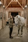 Женщина обнимает лошадь с длинной гривой в конюшне — стоковое фото