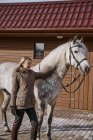 Donna vestita calda con cavallo grigio fuori nel cortile della fattoria — Foto stock