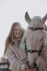 Теплая одетая женщина с серой лошадью на улице во дворе фермы — стоковое фото