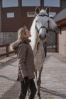 Теплая одетая женщина с серой лошадью на улице во дворе фермы — стоковое фото