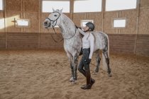 Всадница, стоящая с серой лошадью на круглой арене — стоковое фото