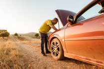 Чоловік вивчає зламаний автомобіль у сільській місцевості — стокове фото