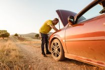 Hombre examinando coche roto en el campo - foto de stock