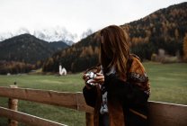 Woman with camera standing near church in mountains — Stock Photo