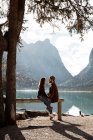 Мужчины и женщины сидят на заборе возле озера и горы — стоковое фото