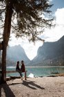 Чоловіки і жінки мандрівники сидять на паркані біля озера і гір — стокове фото