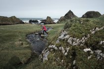 Von oben anonyme Frau genießt erstaunliche malerische Landschaft von Nordirland während der Reise, während sie in der Nähe von schnellen flachen Fluss fließt zu den Gewässern der felsigen Küste — Stockfoto