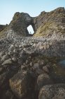 Vista lateral de la hembra en traje caliente de pie en el borde del acantilado dentro de la cueva en el puerto de Irlanda del Norte mirando hacia el mar - foto de stock