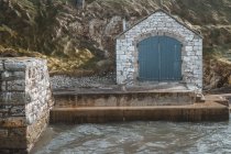 Ancien bâtiment en pierre avec des portes sur la jetée pittoresque du port de Ballintoy sur fond de rochers — Photo de stock