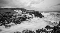 Ondas do mar batendo em rochas e quebrando para baixo a salpicos no dia tempestuoso com nuvens pesadas na costa da Irlanda do Norte — Fotografia de Stock