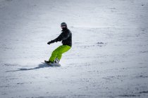 Неузнаваемый человек в наружной одежде и наушниках катается на сноуборде по снежному склону горы на курорте — стоковое фото