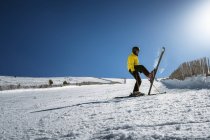 Full body young man in yellow outwear and sunglasses riding skis on snowy mountain slope on sunny winter day on resort — Stock Photo