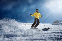 Молодий чоловік у жовтому одязі та сонцезахисних окулярах катається на лижах на сніжному гірському схилі в сонячний зимовий день на курорті — стокове фото