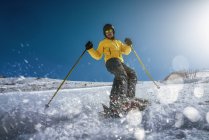 Полное тело юноша в желтой одежде и солнечных очках катается на лыжах по снежному склону горы в солнечный зимний день на курорте — стоковое фото